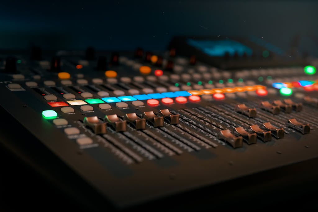 Close-up of a professional sound mixer with colorful glowing controls in a dimly lit studio.