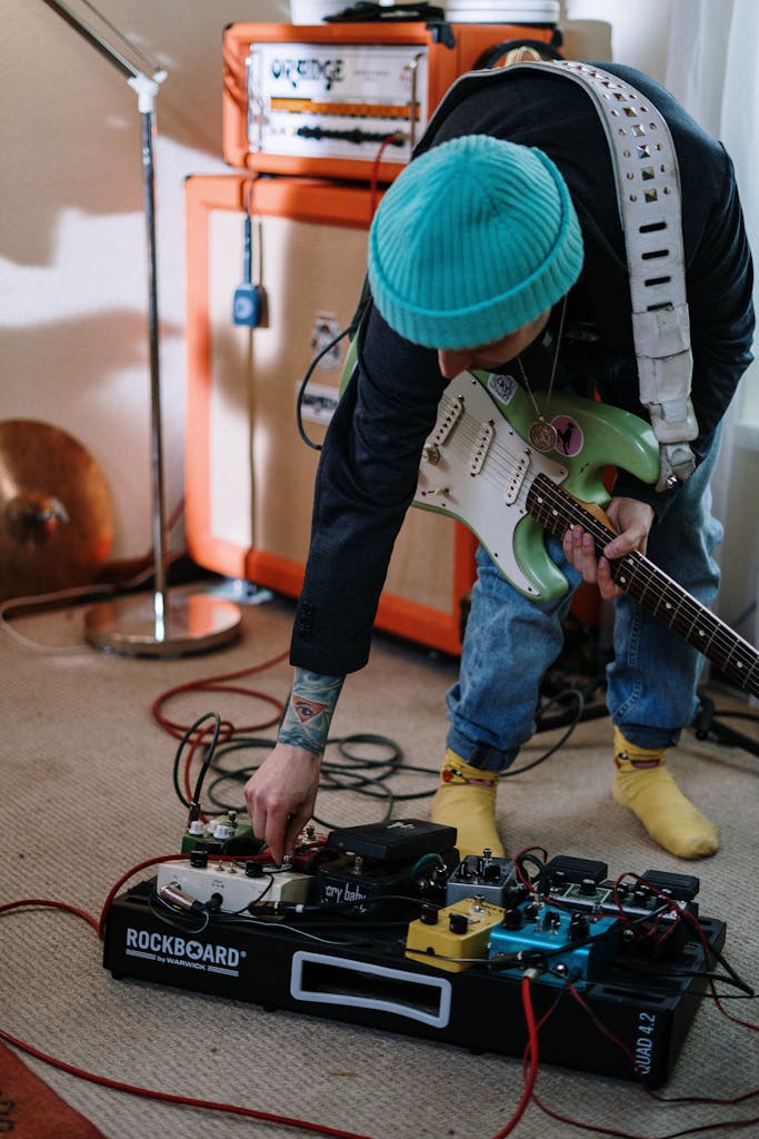 Musician tuning guitar pedals in home studio setup with vibrant colors and casual attire.